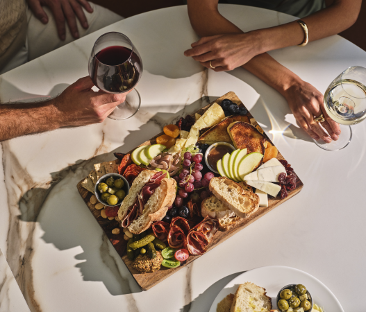 two people sitting at a table enjoying drinks and a charcuterie board