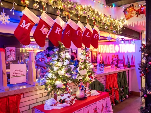 Red stockings spelling out "miracle" are hung above a bar bedecked with holiday decor and Christmas trees at Union Station Denver for the Miracle at Union Station holiday bar pop-up in 2022
