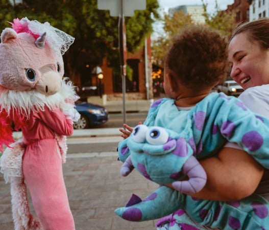 a woman carrying a child waving at someone in a costume